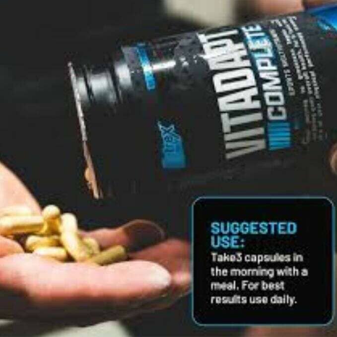 A close-up of a hand holding yellow capsules while a black bottle labeled VITADAPT COMPLETE is tipped, spilling the capsules. A blue text box in the lower right reads 'SUGGESTED USE: Take 3 capsules in the morning with a meal.