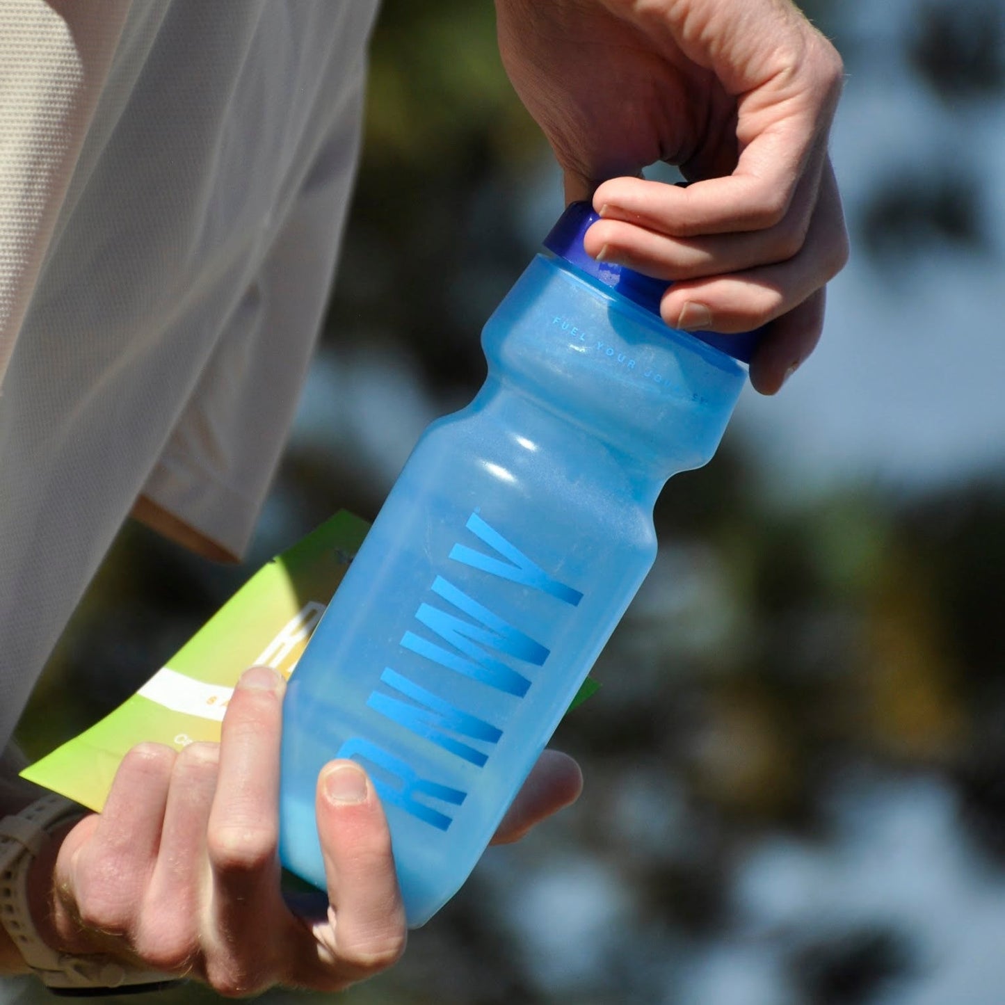 Person holding a blue water bottle with a blurred natural background