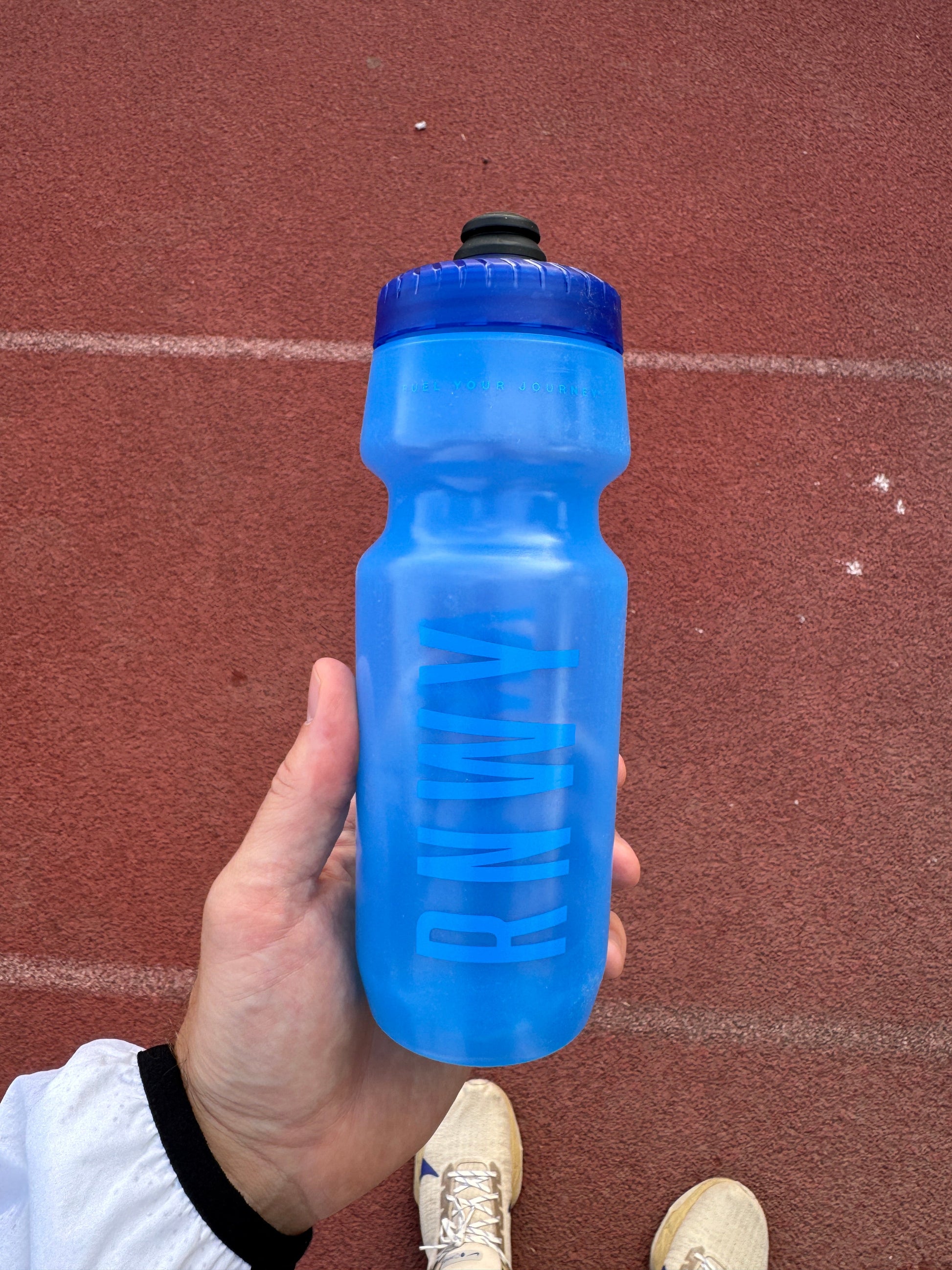 Hand holding a blue water bottle with a red track surface in the background