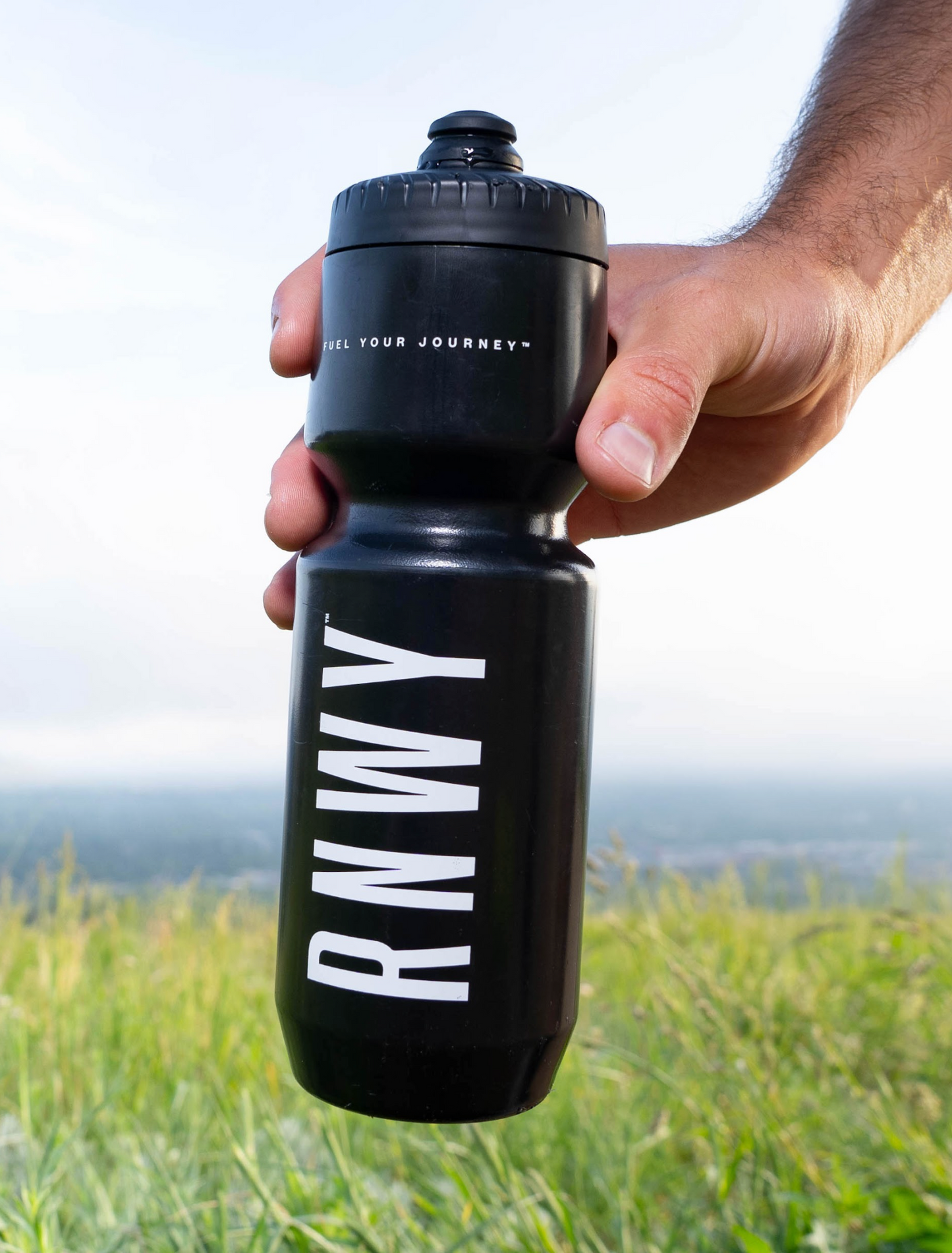 Black water bottle with 'RNWY' branding held by a person outdoors.