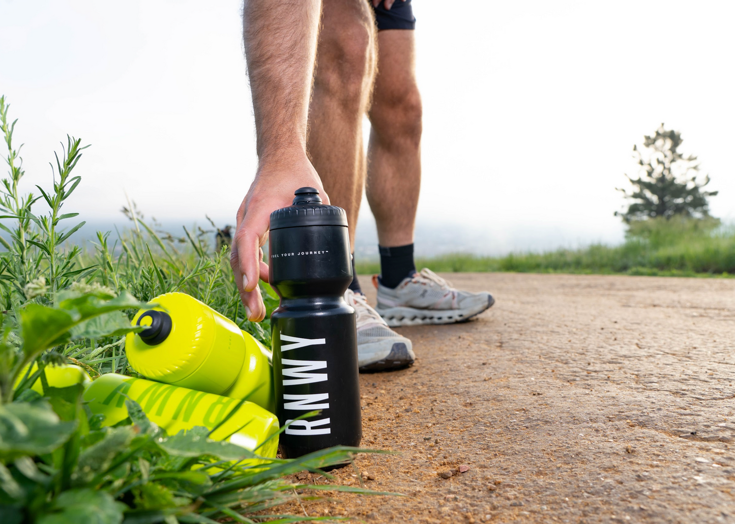 Person holding a black water bottle with 'Kuma' branding on a trail