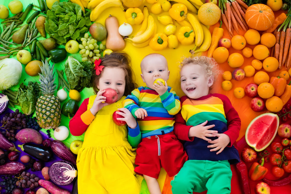 Three children surrounded by a colorful arrangement of fruits and vegetables.